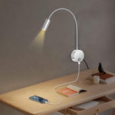 Wall-mounted reading lamp on a wooden desk with a smartphone and book.